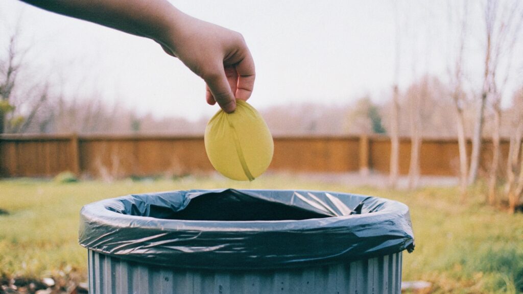 A hand putting a deflated balloon into a trash can
