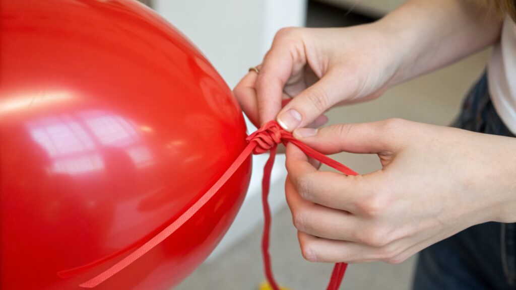 Close-up of hands tying a latex balloon knot