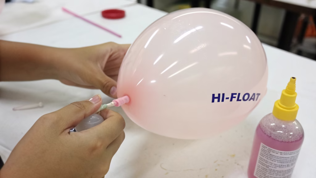 A hand applying HI-FLOAT treatment inside a latex balloon before inflation