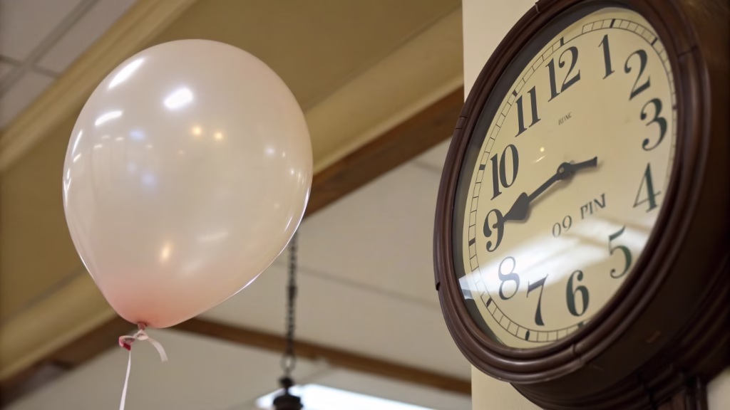 A close-up shot of a clock next to a floating latex balloon